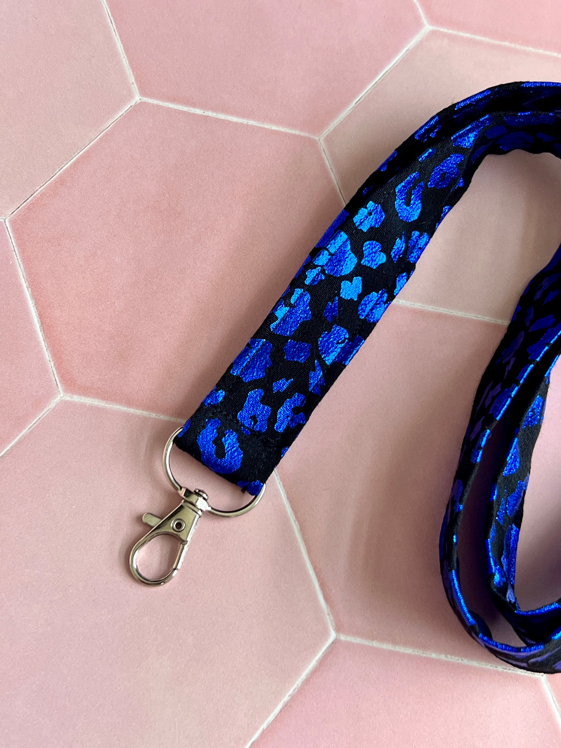 Close-up of handmade black lanyard with shimmering blue foil leopard pattern, featuring secure D-ring for everyday essentials