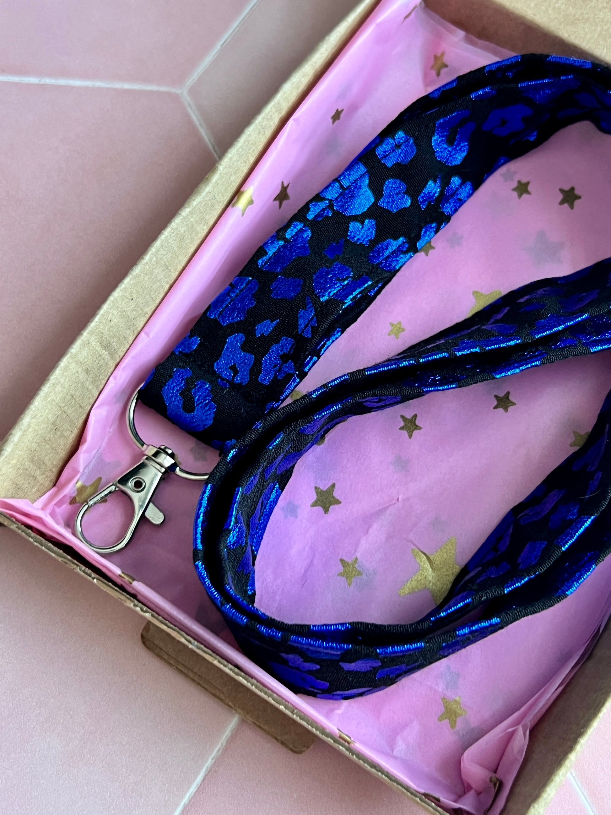 Close-up of handmade black and blue foil leopard print lanyard with D-ring, packaged in pink and gold star tissue paper