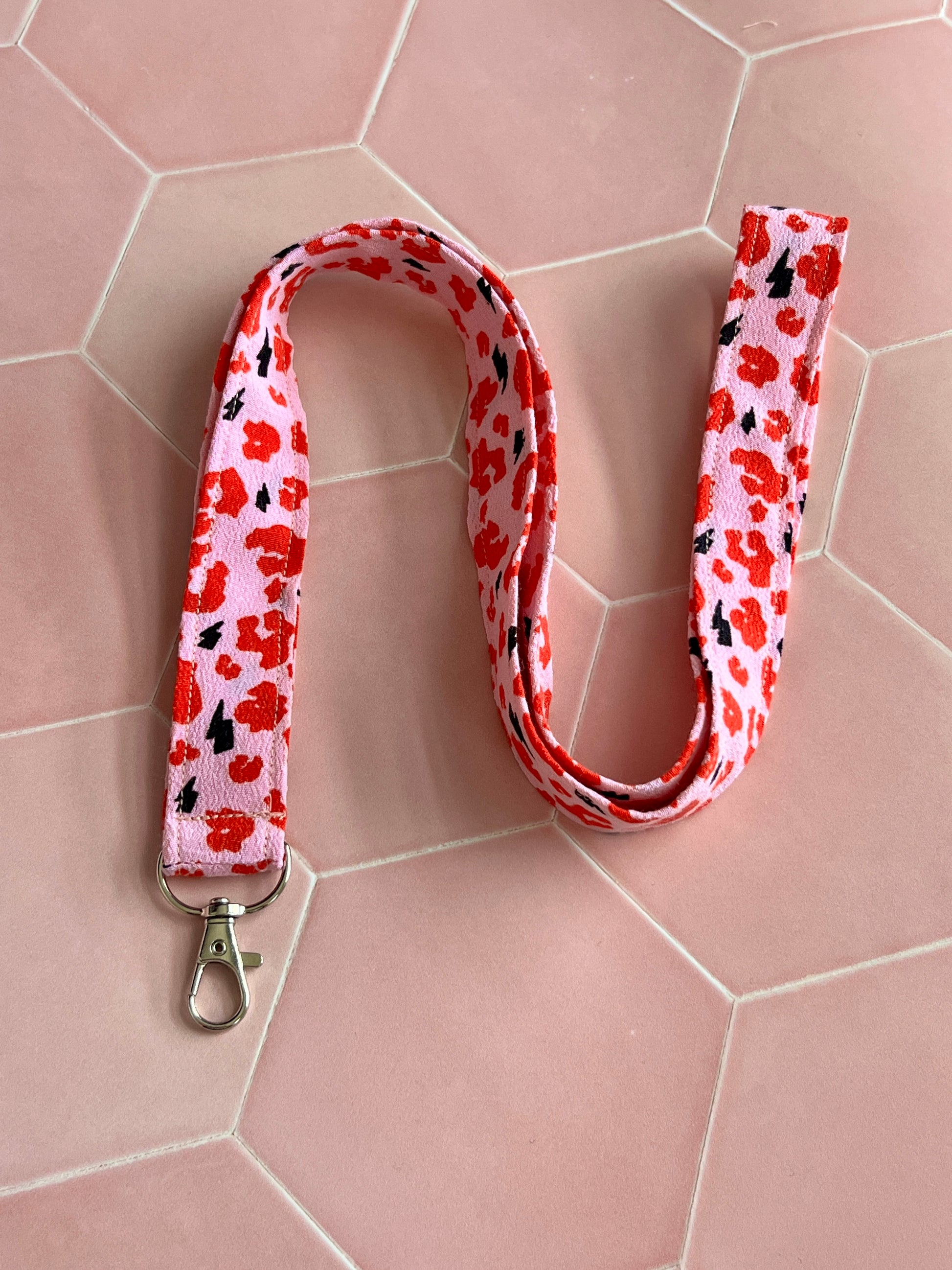 Flat lay of bold pink and red leopard print lanyard, handmade fabric design with D-ring attachment for keys and work badges